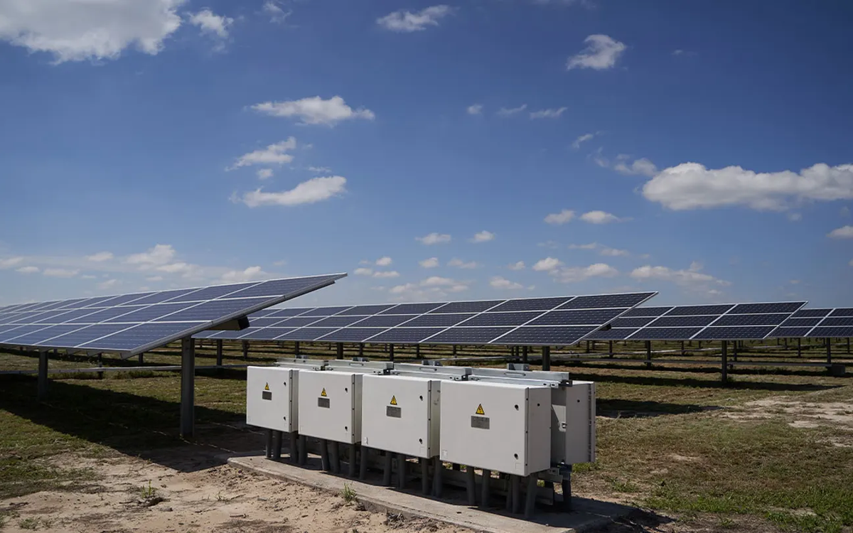 Rows of solar panels in a field with grid-connected power inverters in the foreground