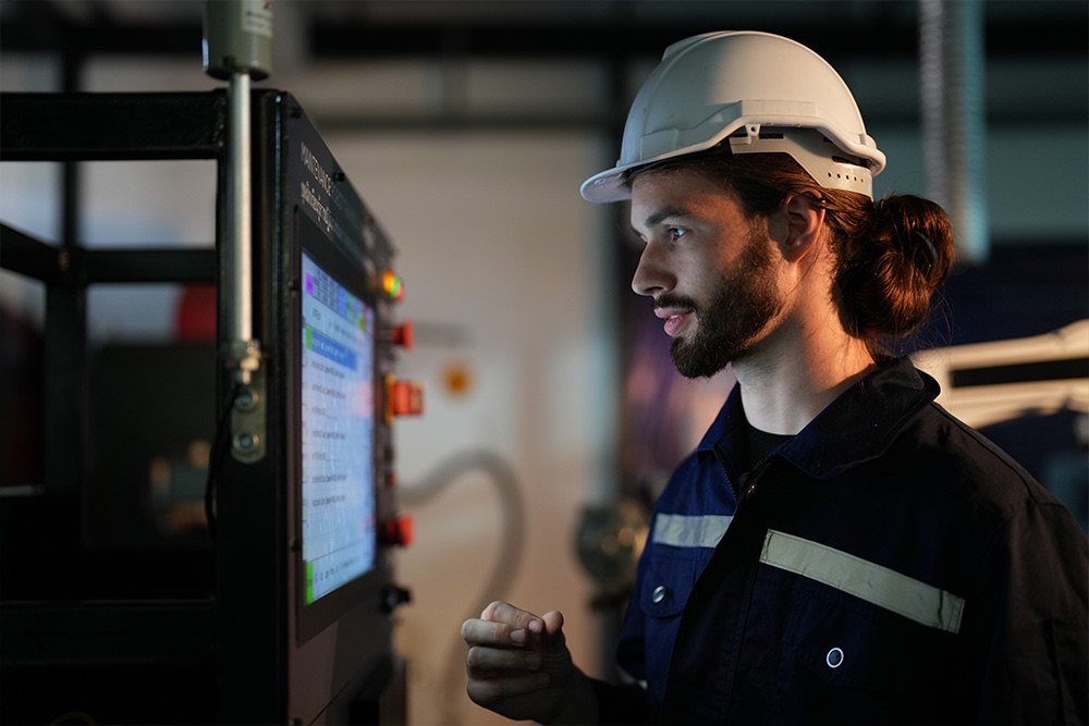 A worker in a hard hat using an industrial touchscreen control panel